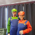 Smiling man in Luigi L costume, woman in Mario M costume.