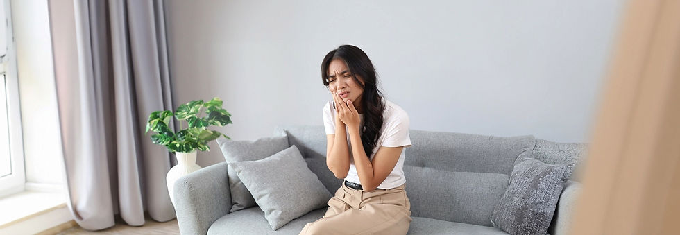 A young woman sitting on a sofa at home touches her cheek,