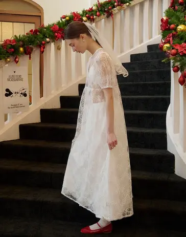 Young woman in white dress, veil, walks down Christmas-decorated stairs.