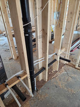 Black plumbing pipes rough-in within new wood wall framing construction.