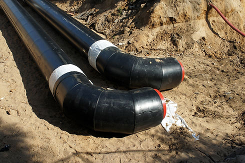 Large black pipes with red caps in a dirt trench