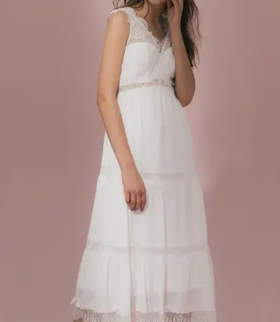 Woman wearing white tiered lace dress, Bridal Wear, standing against pink background.