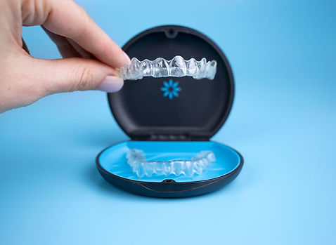 Hand holding an Invisalign clear aligner over its case