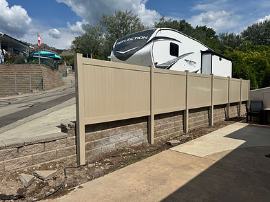 Long tan privacy fence alongside a retaining wall with large RV.