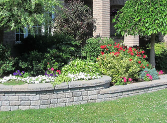 Landscaped garden with a curved stone retaining wall, colorful flowers, greenery.