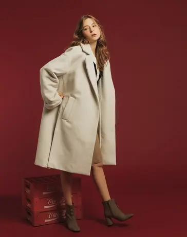 Stylish woman in beige long coat and boots on red background.