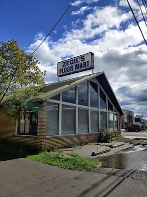 Building with "ZEGIL'S FLOOR MART" sign, large windows, cloudy sky.