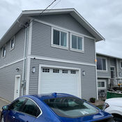 Two-story gray building with a garage, windows, and parked cars outside