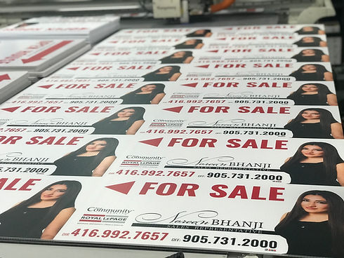 Multiple 'FOR SALE' signs with realtor's photos and phone numbers