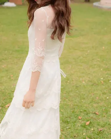 Woman in elegant white lace Bridal Wear dress standing in green grass.