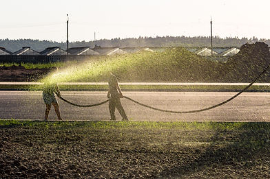 Two workers hydroseeding a field, spraying green mixture on barren ground.