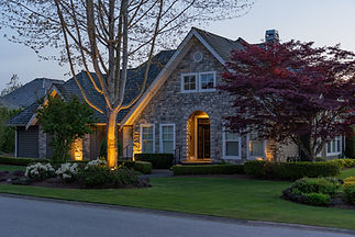 Large stone house and garden, beautifully lit by evening landscape lights.