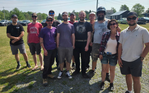 Eleven casual people smiling outdoors on a bright sunny day.