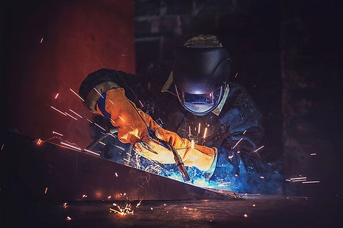 Welder in safety gear performing steel fabrication with sparks.