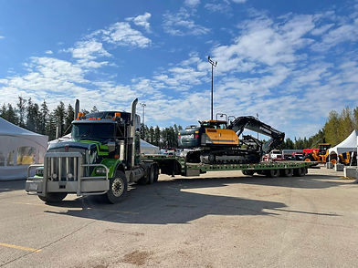 Green semi-truck hauling a yellow excavator on trailer