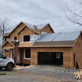 New two-story house under construction with plywood sheathing, attached garage, cloudy sky.