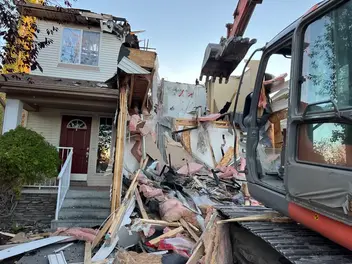 Heavy excavator actively demolishing a house, leaving extensive construction debris.