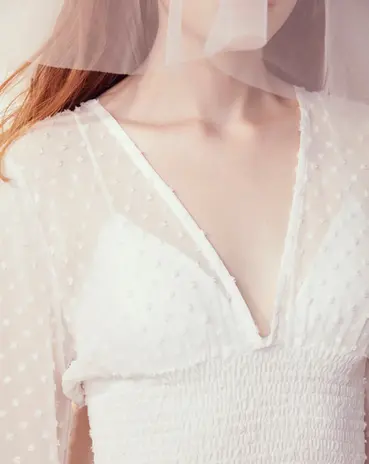 Woman wears elegant white V-neck dress with sheer veil.