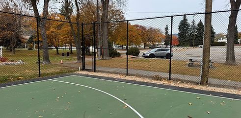 Green basketball court, black fence, autumn park, walking path, parking lot.
