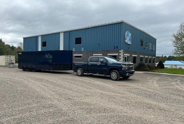 Blue pickup truck towing a trailer outside a blue building.