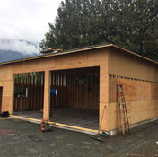 Garage construction, wooden frame, two bays, ladder, under cloudy sky and mountain backdrop.