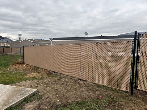 Long chain-link fence with tan privacy slats in a residential backyard.