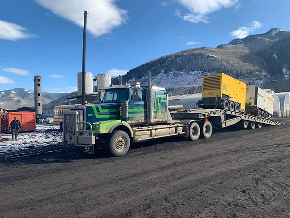 Green semi-truck hauling equipment at industrial site
