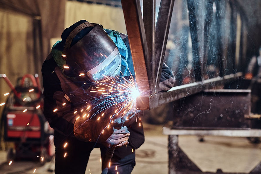 Welder joining metal parts in a steel fabrication workshop.