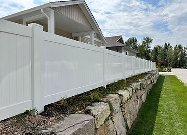 White vinyl fence on stone retaining wall shielding residential property.