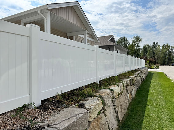 Long white privacy fence on stone retaining wall under cloudy sky.