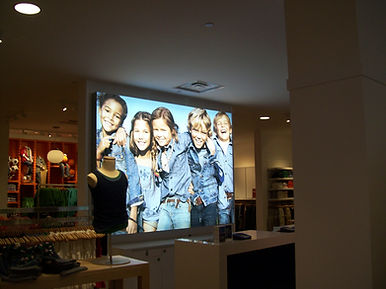Retail store with large lit display of smiling children in denim