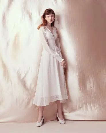 Young woman models elegant white long-sleeve v-neck midi dress.