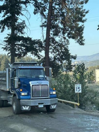 Blue dump truck and trailer on dirt road, 15 mph sign