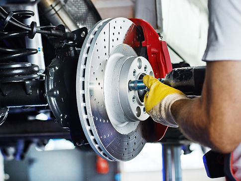 Mechanic's hands in yellow gloves working on a car's disc brake.