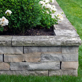 Stacked stone retaining wall with white flowers and lush green grass.