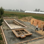 Workers building a concrete swimming pool with wooden frames near a field