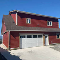Red house with white garage doors and windows, suites and additions, mountain backdrop.