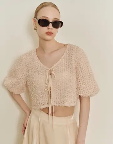 Woman wearing light pink cropped eyelet cardigan and dark sunglasses.