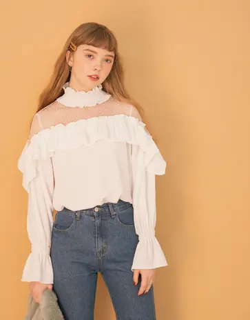 Young woman in white ruffled blouse and blue jeans looking forward.