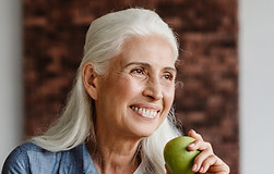 Smiling senior woman holding a green apple, sitting at table with apple