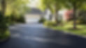 Freshly paved asphalt driveway leading to a white house