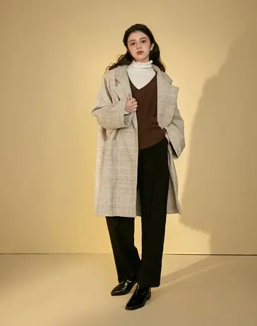 Woman wearing a plaid trench coat, white turtleneck, brown top, black pants.