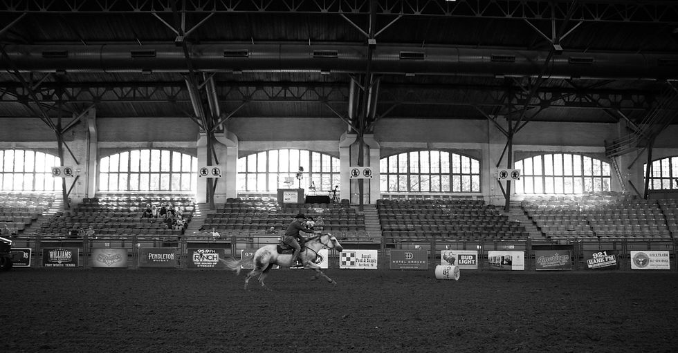 A black and white photo of the inside of a rodeo coliseum with a barrel racer running through the middle