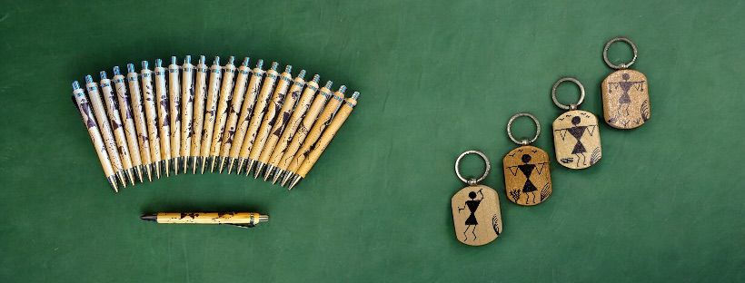 Handcrafted wooden Warli art pens and keychains displayed together, showcasing traditional Indian tribal art on functional products.