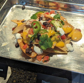 A tray of chicken nachos loaded with cheese, beans, tomatoes, and other toppings.