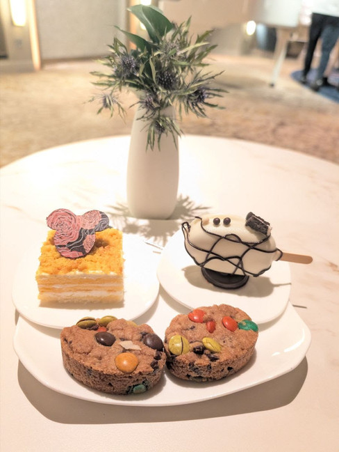 A selection of complimentary desserts and treats in the Disney Adventure Concierge Lounge, including cookies, layered cake, and a Mickey-shaped frozen dessert served on a white table.
