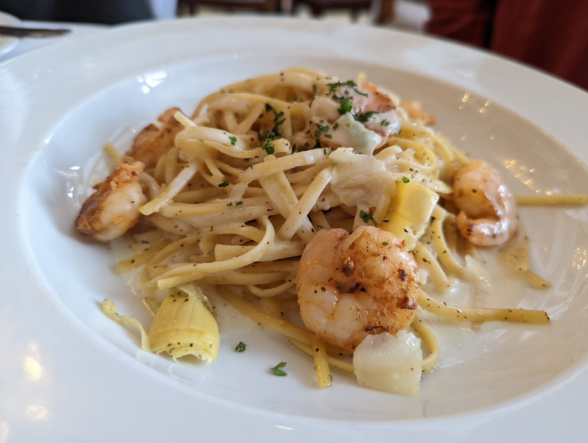 A white plate with a serving of pasta topped with shrimp. The pasta appears to be linguine with a light-colored sauce.