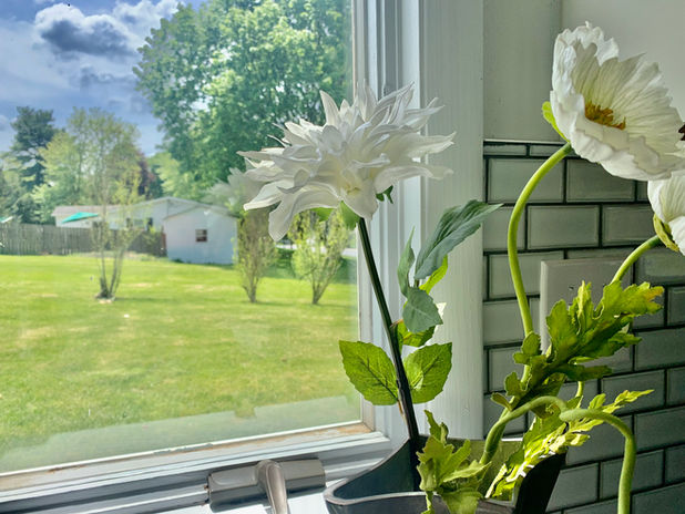 Kitchen with a pretty window view accentuated with white flowers in a silver vase.