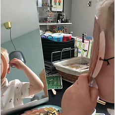 A preschooler examining their paper monkey mask in a mirror while experimenting with animal sounds.