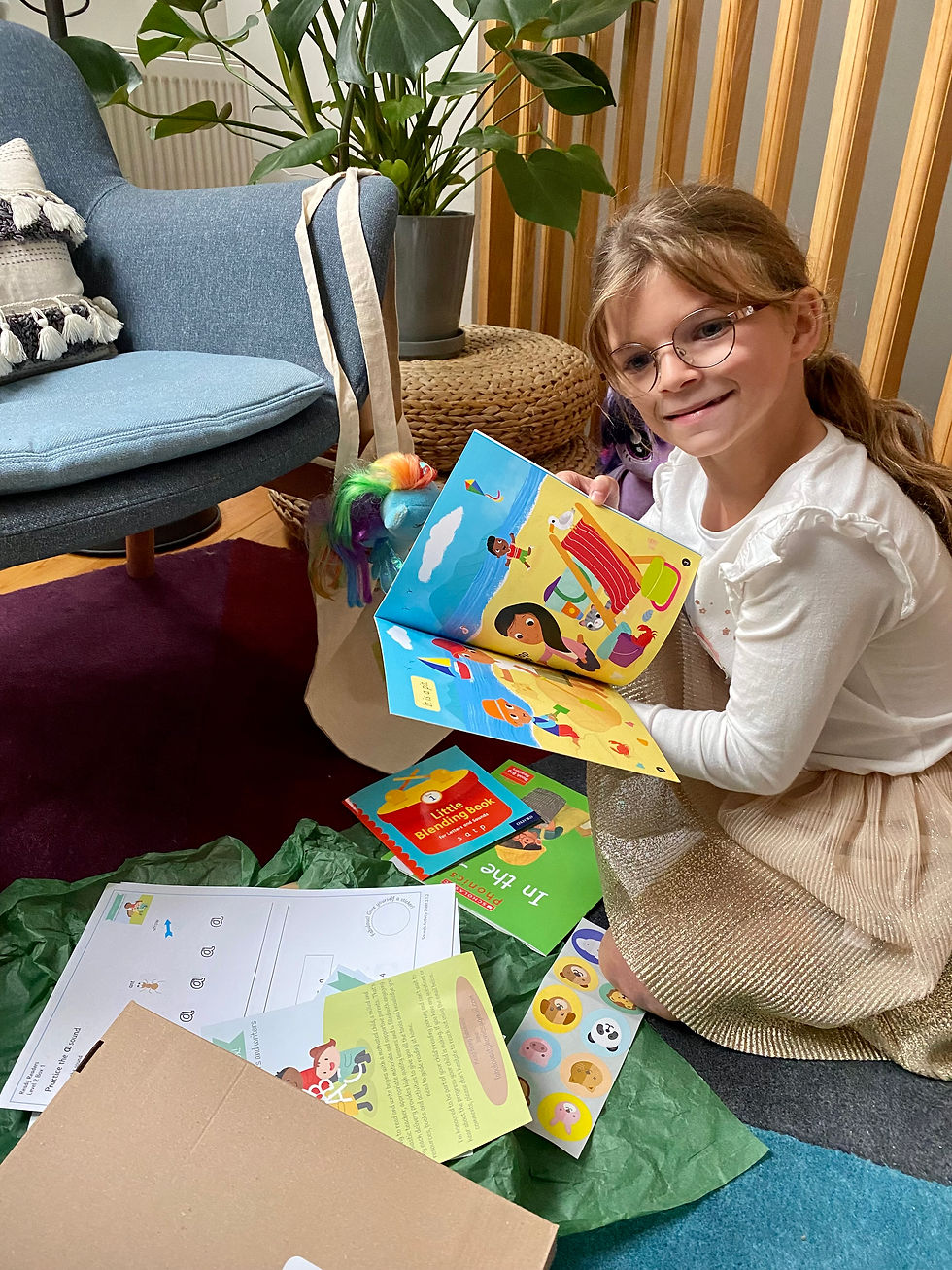 A child sitting on a rug surrounded by books and cuddly toys, enjoying a calm reading moment.